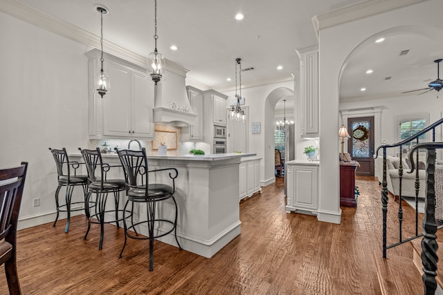 kitchen with arched walkways, stainless steel appliances, light countertops, hanging light fixtures, and white cabinetry