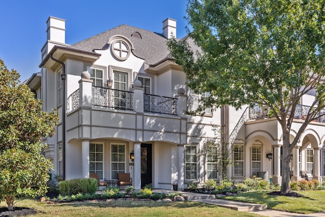 view of front of house featuring a shingled roof, a balcony, a chimney, a porch, and stucco siding