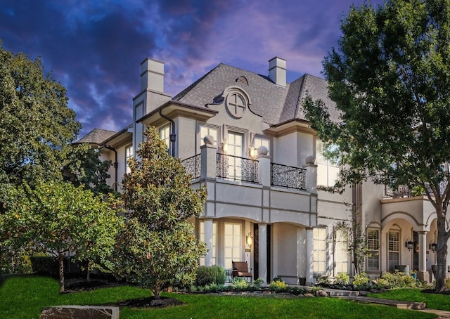 view of front of home featuring a chimney, a balcony, and stucco siding