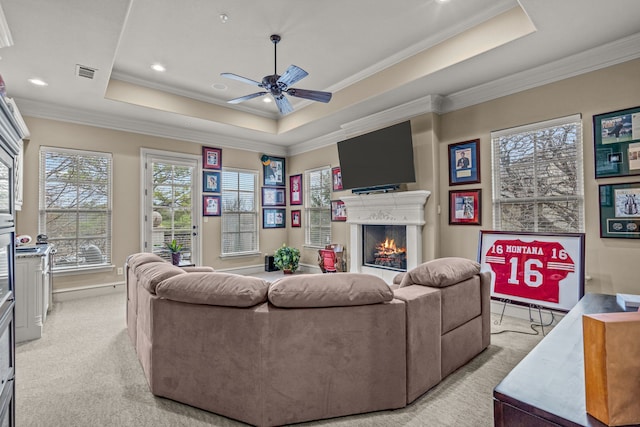 living room featuring light carpet, visible vents, a lit fireplace, a tray ceiling, and crown molding