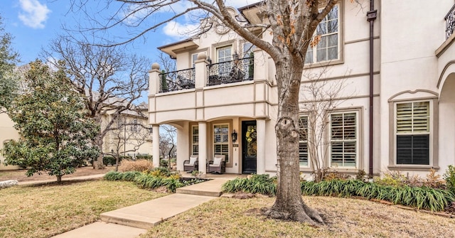 view of front of home with a front yard, a balcony, and stucco siding