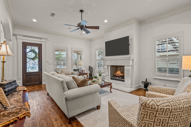 living area with visible vents, ceiling fan, ornamental molding, wood finished floors, and a lit fireplace