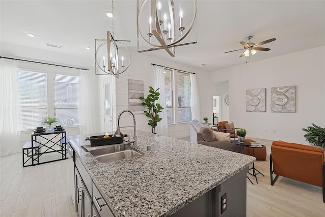 kitchen featuring pendant lighting, a center island with sink, light wood-style flooring, open floor plan, and a sink