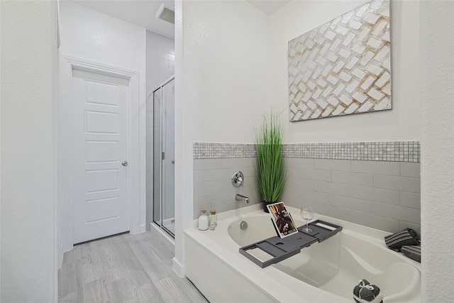 bathroom with a stall shower, a garden tub, and wood finished floors