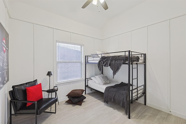 bedroom with vaulted ceiling, light wood finished floors, and a decorative wall