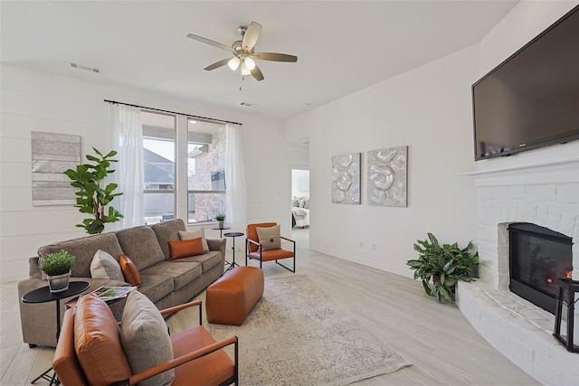 living room featuring baseboards, visible vents, a ceiling fan, light wood-style floors, and a fireplace