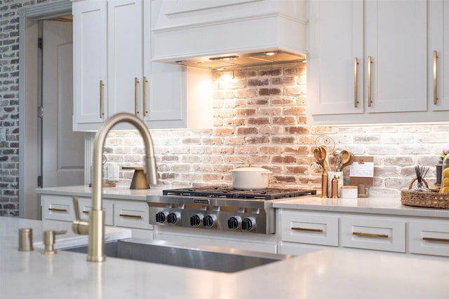 kitchen featuring custom exhaust hood, white cabinets, brick wall, and stainless steel gas stovetop