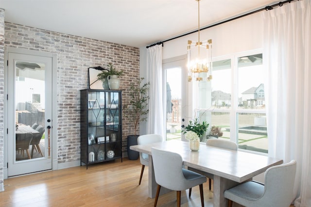 dining space featuring a chandelier, brick wall, and light wood finished floors