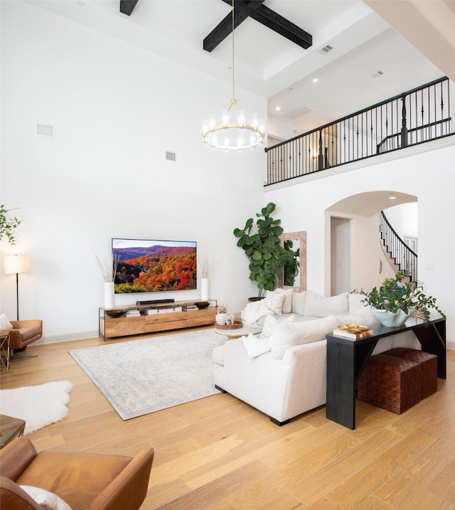 living area featuring wood finished floors, visible vents, arched walkways, a towering ceiling, and a chandelier