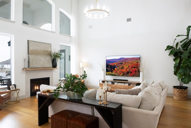 living room with wood finished floors, visible vents, a high ceiling, a lit fireplace, and a chandelier