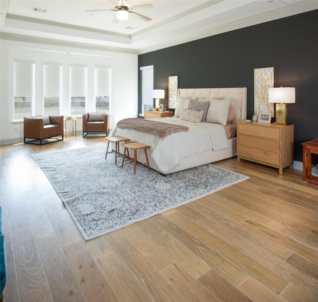 bedroom featuring a raised ceiling, wood finished floors, visible vents, and ornamental molding