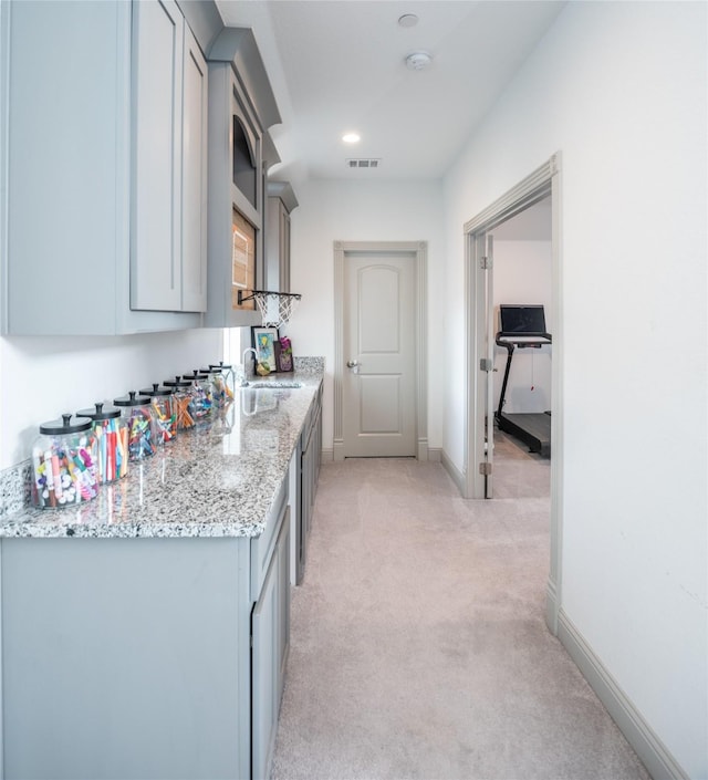 kitchen featuring visible vents, light carpet, gray cabinetry, baseboards, and light stone countertops