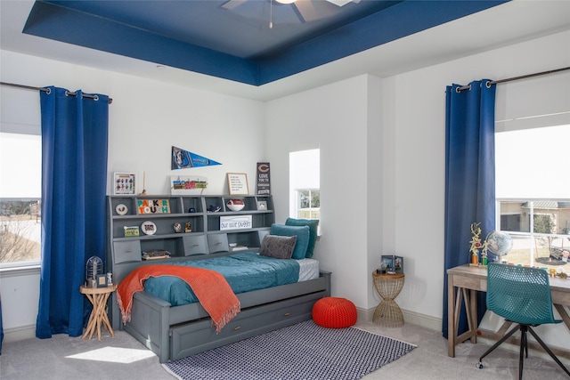 carpeted bedroom featuring baseboards, a raised ceiling, and ceiling fan