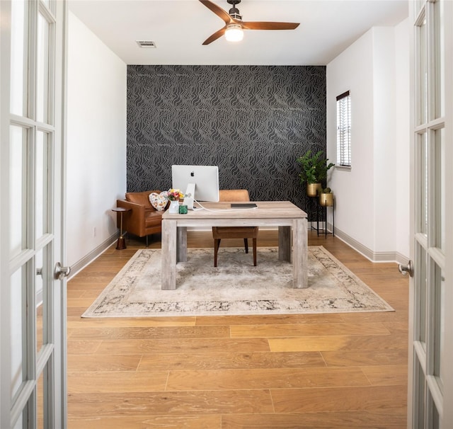 office space featuring wallpapered walls, an accent wall, baseboards, and wood finished floors