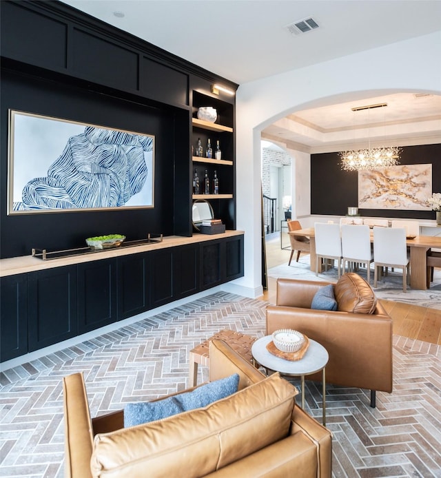 living room with visible vents, a tray ceiling, arched walkways, an inviting chandelier, and brick floor