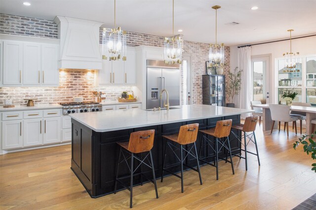 kitchen with a sink, custom exhaust hood, appliances with stainless steel finishes, and brick wall