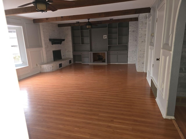 unfurnished living room with a large fireplace, ceiling fan, beamed ceiling, and a decorative wall