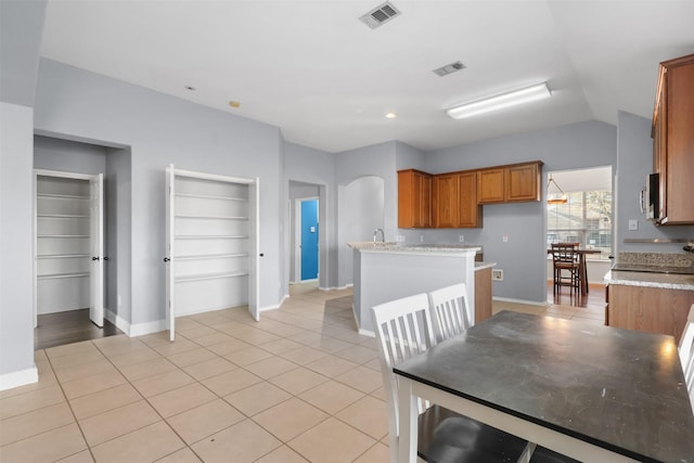 kitchen featuring arched walkways, brown cabinets, visible vents, and light tile patterned floors