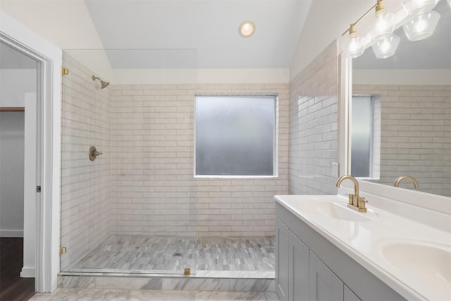 bathroom with double vanity, vaulted ceiling, a sink, and tiled shower