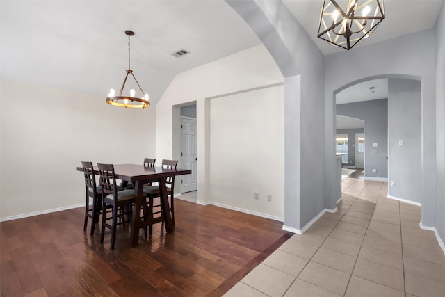 dining area featuring arched walkways, visible vents, vaulted ceiling, wood finished floors, and a chandelier