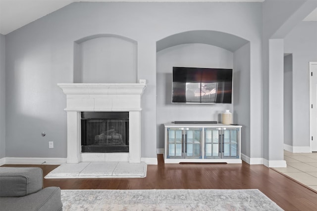 living room featuring a fireplace with raised hearth, vaulted ceiling, wood finished floors, and baseboards