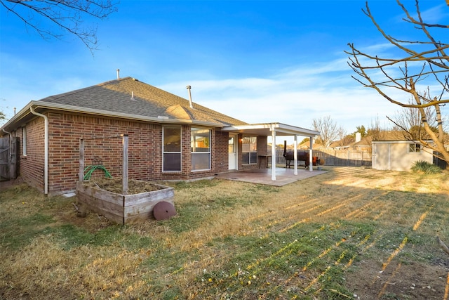 rear view of house featuring an outbuilding, a patio, brick siding, a yard, and roof with shingles