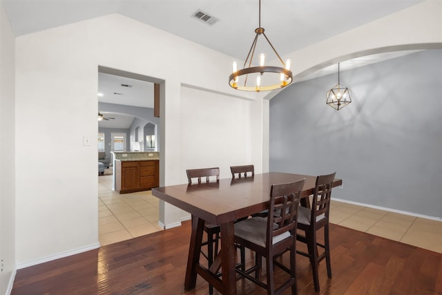 dining space with light wood finished floors, baseboards, visible vents, arched walkways, and lofted ceiling