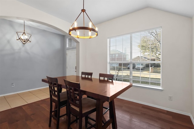 dining room with dark wood-style floors, arched walkways, vaulted ceiling, and an inviting chandelier