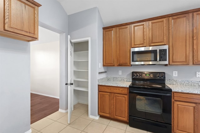 kitchen featuring light tile patterned floors, light stone counters, black range with electric stovetop, brown cabinetry, and stainless steel microwave