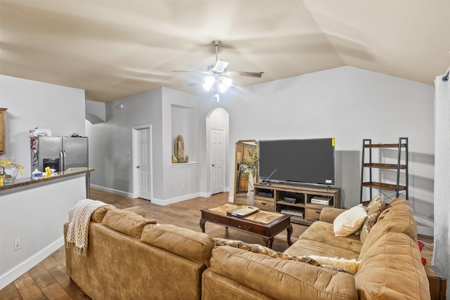 living area featuring baseboards, arched walkways, a ceiling fan, wood finished floors, and vaulted ceiling