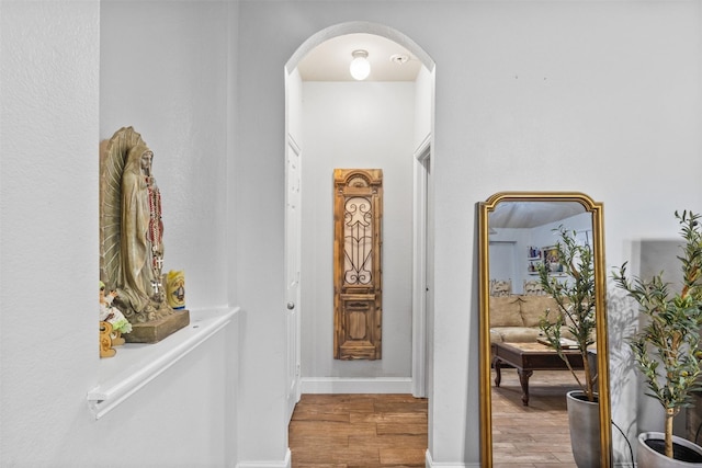 hallway featuring light wood-type flooring, arched walkways, and baseboards