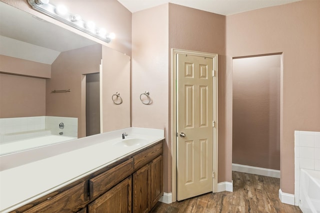 bathroom featuring a garden tub, baseboards, wood finished floors, and vanity