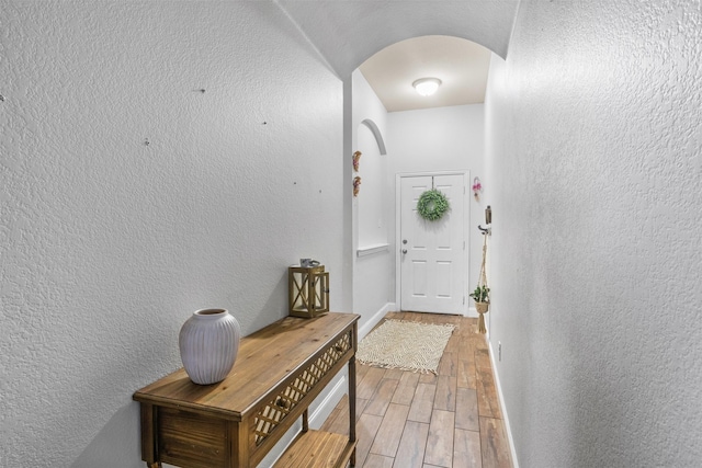 doorway featuring arched walkways, a textured wall, baseboards, and wood tiled floor