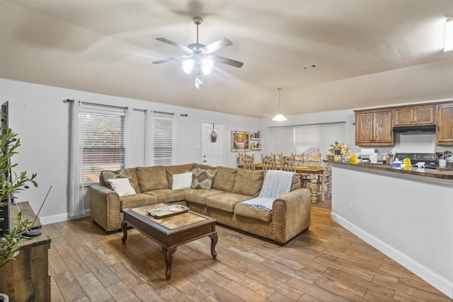 living area with light wood finished floors, baseboards, visible vents, a ceiling fan, and vaulted ceiling