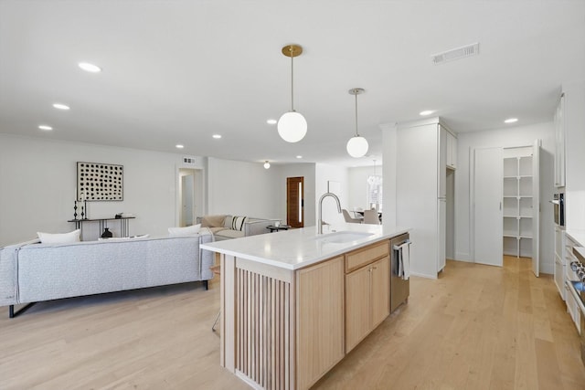 kitchen featuring an island with sink, open floor plan, light countertops, light brown cabinetry, and a sink