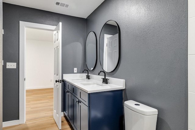 bathroom featuring double vanity, wood finished floors, a sink, and visible vents