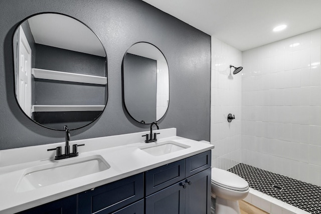 full bathroom featuring toilet, double vanity, a sink, and tiled shower