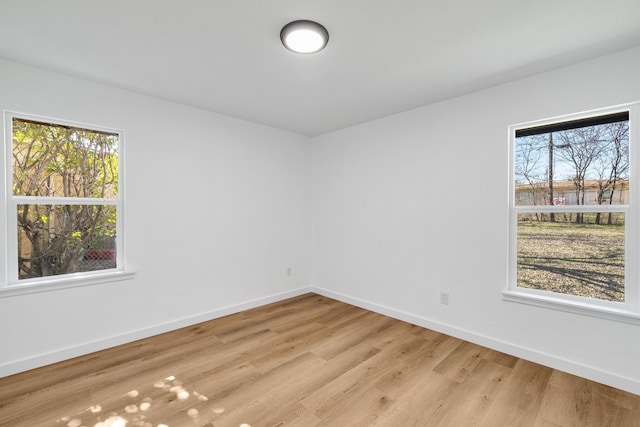 empty room with baseboards, plenty of natural light, and light wood finished floors