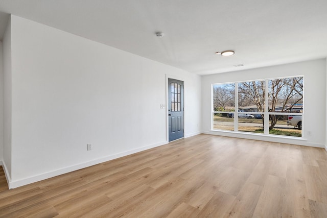 spare room featuring light wood finished floors, visible vents, and baseboards