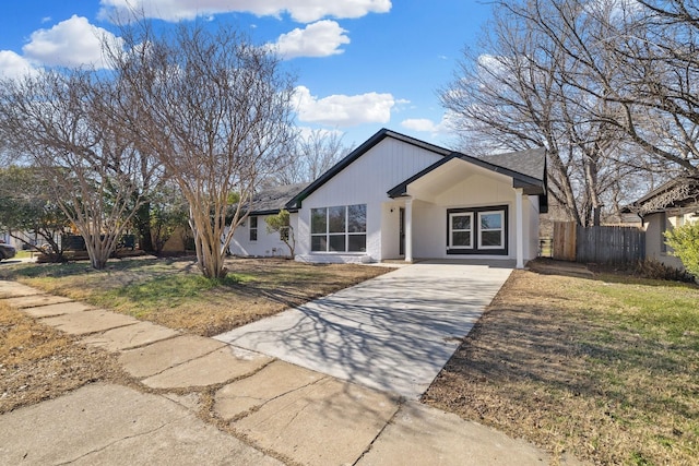 view of front of property featuring concrete driveway, fence, and a front lawn