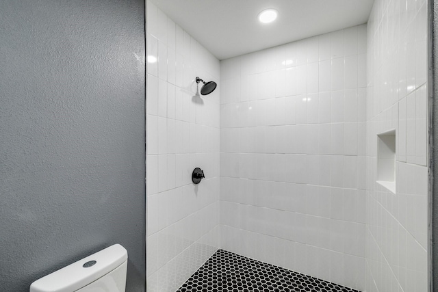 full bath with a textured wall, a tile shower, and toilet