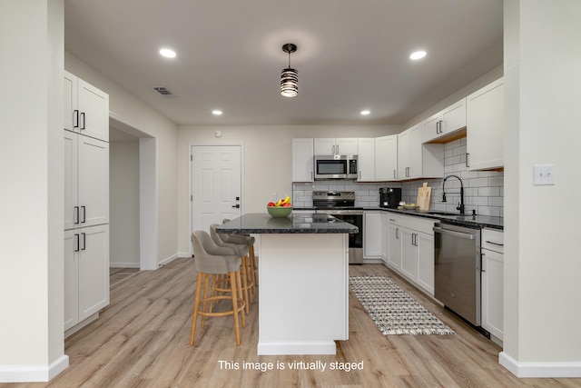 kitchen featuring visible vents, decorative backsplash, stainless steel appliances, light wood-type flooring, and a sink