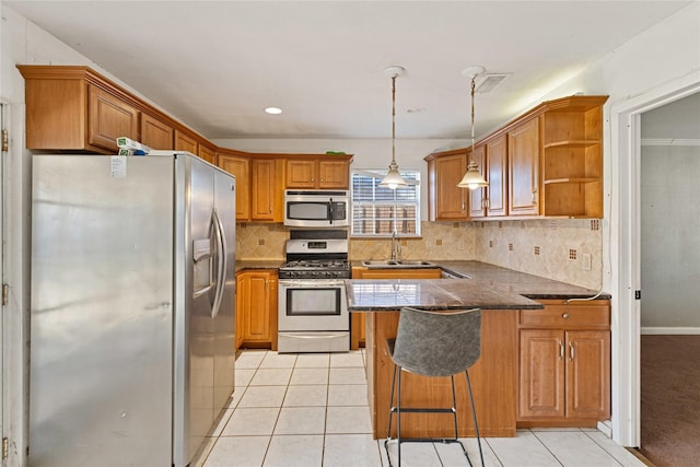 kitchen with dark countertops, appliances with stainless steel finishes, a breakfast bar, a peninsula, and a sink