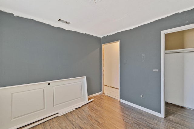 unfurnished bedroom with a closet, visible vents, baseboards, and wood finished floors