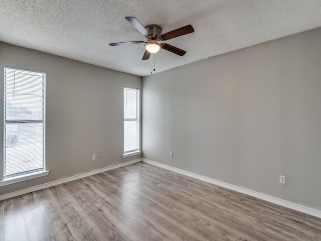 spare room featuring light wood-type flooring, ceiling fan, baseboards, and a textured ceiling