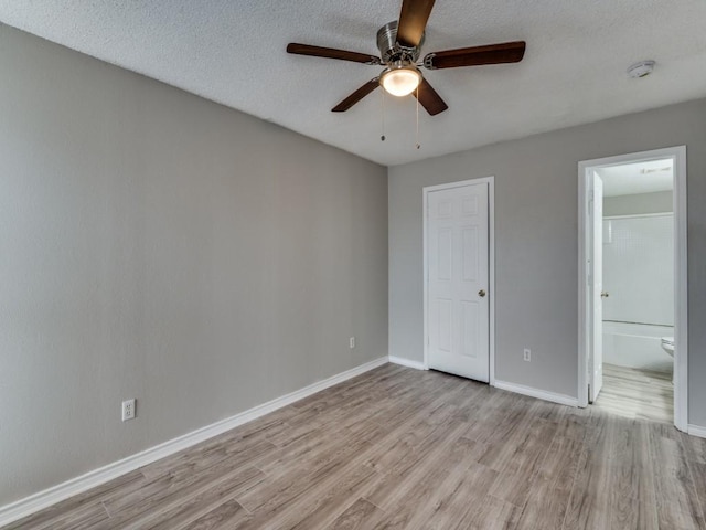 unfurnished bedroom with a textured ceiling, connected bathroom, a ceiling fan, baseboards, and light wood-type flooring