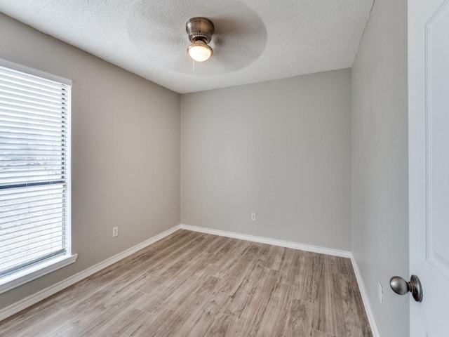 empty room featuring ceiling fan, light wood-style flooring, baseboards, and a textured ceiling