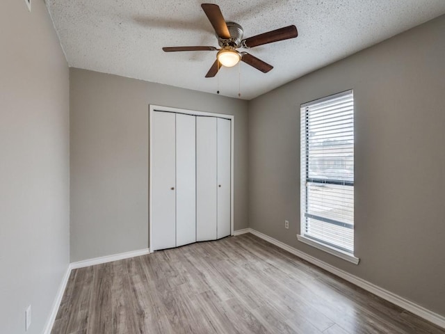 unfurnished bedroom featuring ceiling fan, a textured ceiling, baseboards, light wood-style floors, and a closet