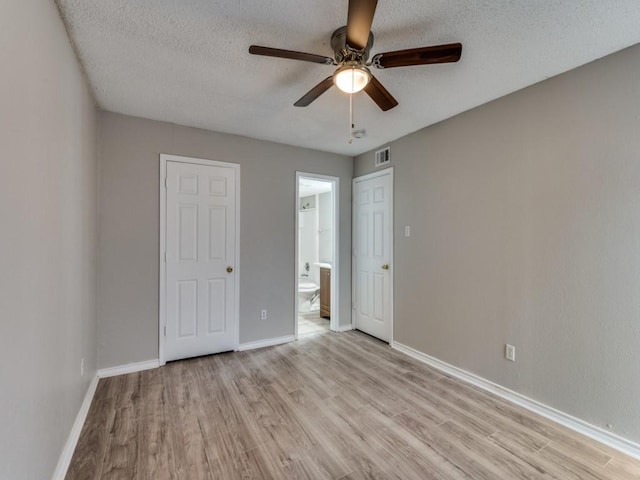 unfurnished bedroom with a textured ceiling, visible vents, baseboards, light wood-style floors, and ensuite bath