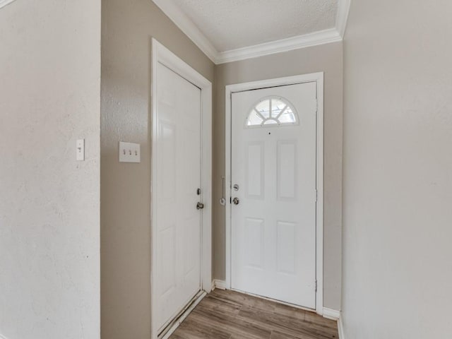 doorway to outside with baseboards, a textured ceiling, wood finished floors, and crown molding